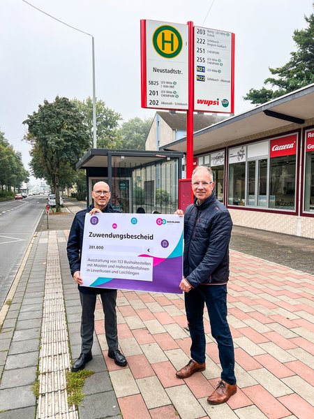 Dr. Norbert Reinkober überreicht den Förderbescheid an wupsi-Geschäftsführer Marc Kretkowski an der Haltestelle Neustadtstraße. (© wupsi GmbH)